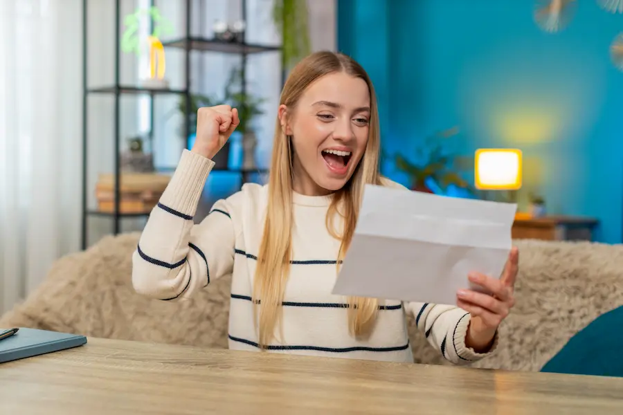 Mulher sorrindo e comemorando ao ler uma carta em casa, representando a alegria da contemplação e o uso da carta de crédito no Consórcio.